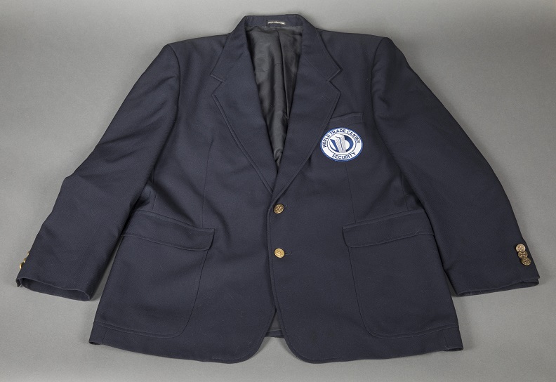 Navy blue blazer with brass button and an indiscernible circular white and blue patch sewn on left pocket.