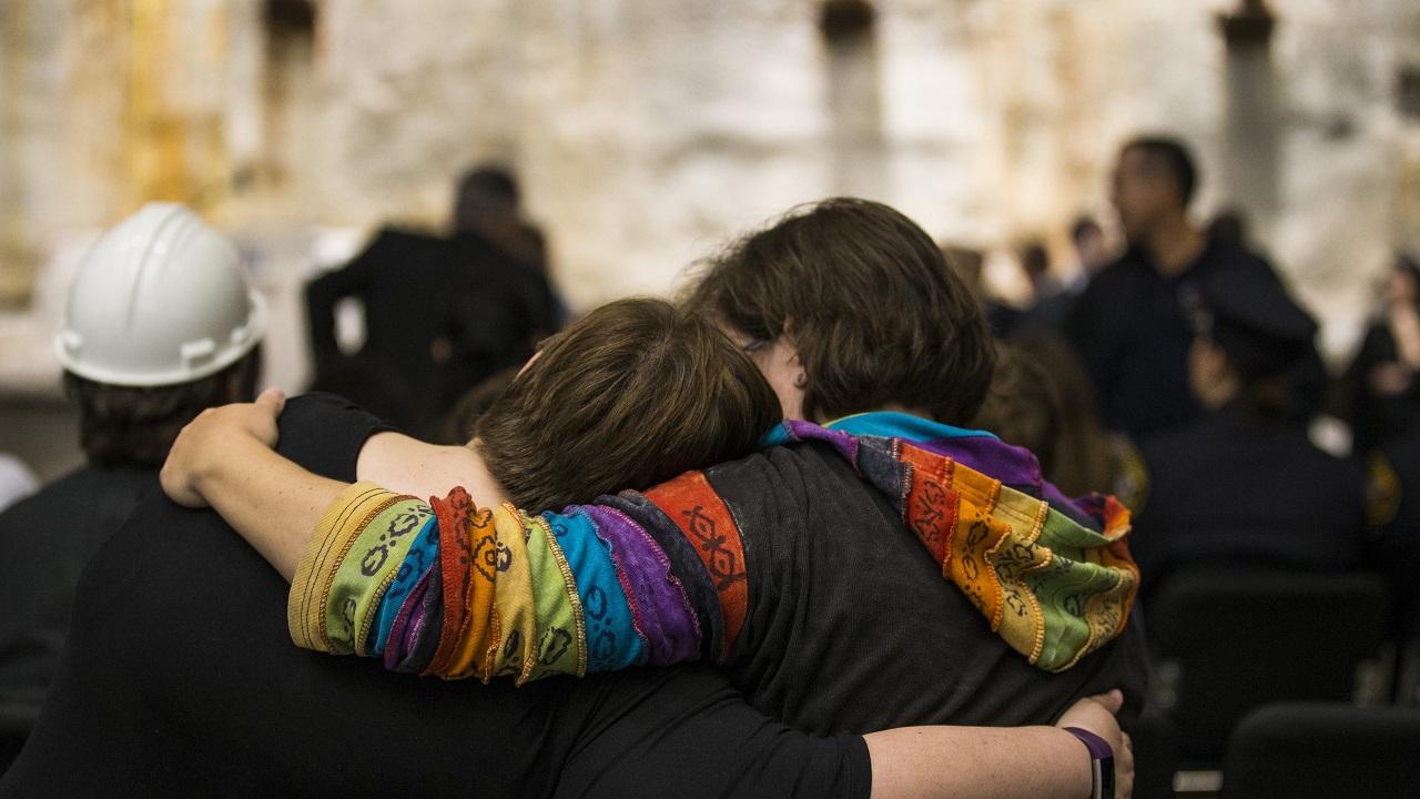 Two women embrace while standing in a crowd beside the slurry wall in Foundation Hall.